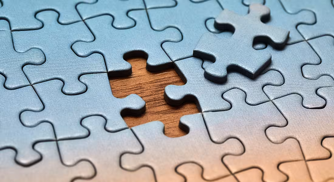 Blue jigsaw puzzle on a wooden table with one last piece missing, symbolising a skills gap.