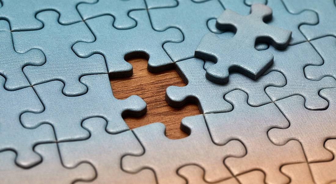 Blue jigsaw puzzle on a wooden table with one last piece missing, symbolising a skills gap.