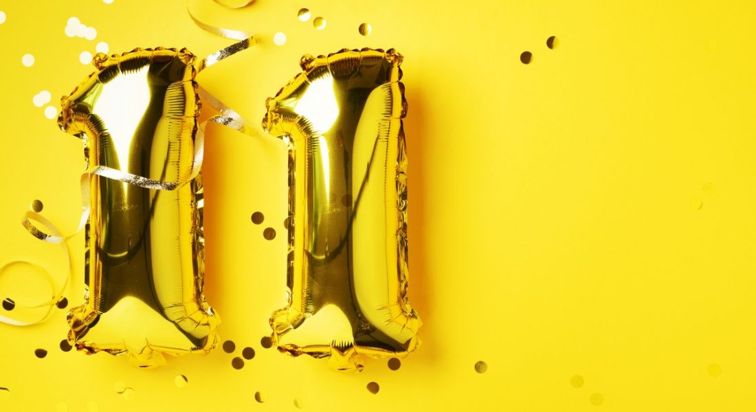 Gold foil balloons in the shape of the number 11 are against a bright yellow background with confetti.