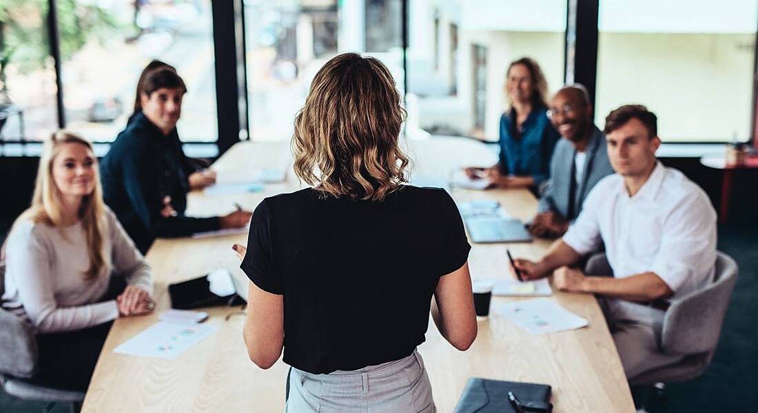 A business woman addressing a group of colleagues sitting around a table.