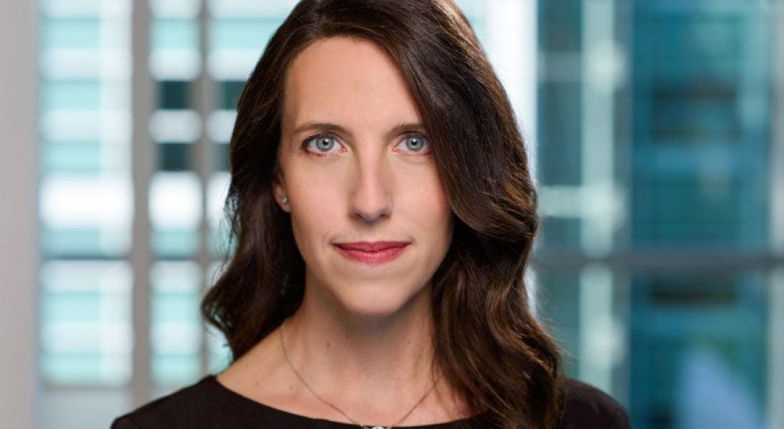 Headshot of Ali Rayl, a woman with long dark hair pictured in a blue-tinged glass-panelled office.