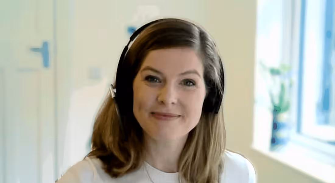 Emma Mullan of Liberty IT is sitting with headphones on and smiling into the camera.