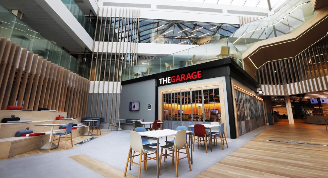 Interior of a modern building’s atrium with daylight streaming through a glass ceiling and a closed off area called ‘The Garage’.