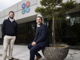 Mammoth co-founders Paul Martin and Jeremy Poots, wearing business-casual attire, stand in a brightly lit office space.