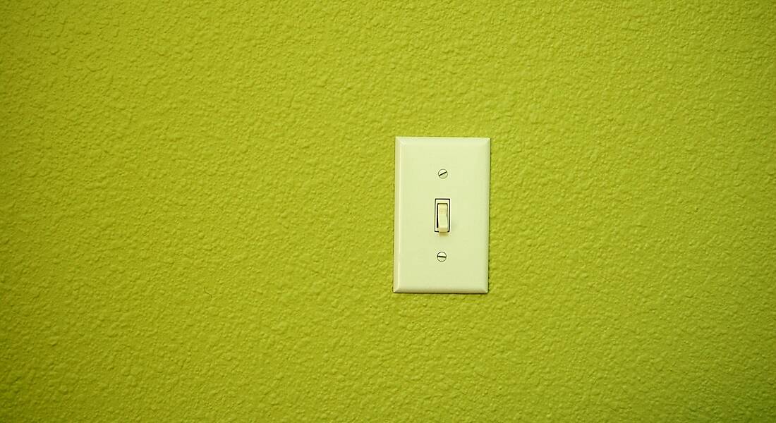 A light switch on a bright green wall.