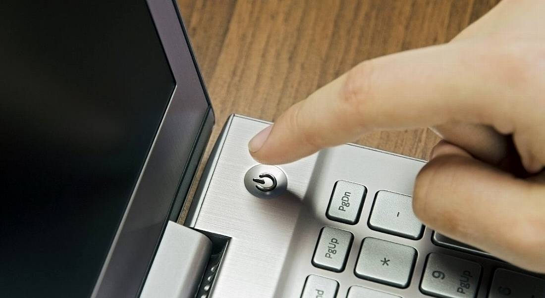 Close-up view of a finger about to hit the off button on a laptop.