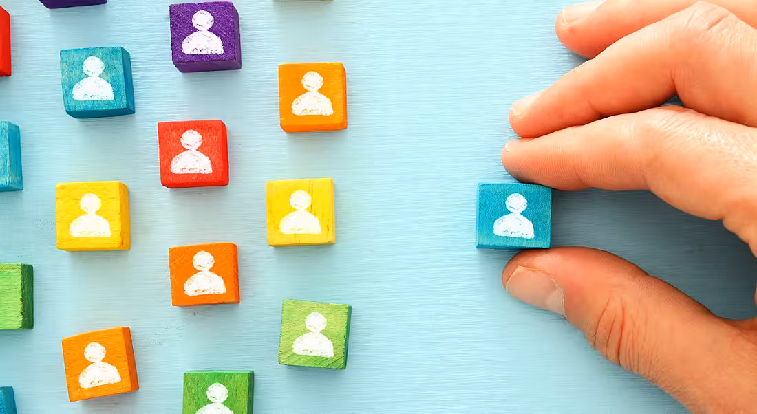 A person's hand is arranging colourful blocks with people silhouettes on them.