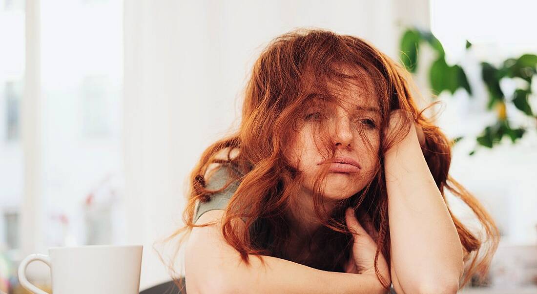 A woman with red hair is sitting at a desk with her head in her hands as if she is dreading coming back to work.