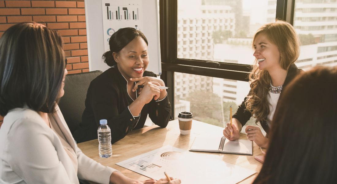 Women in leadership are sitting by a window in a boardroom.