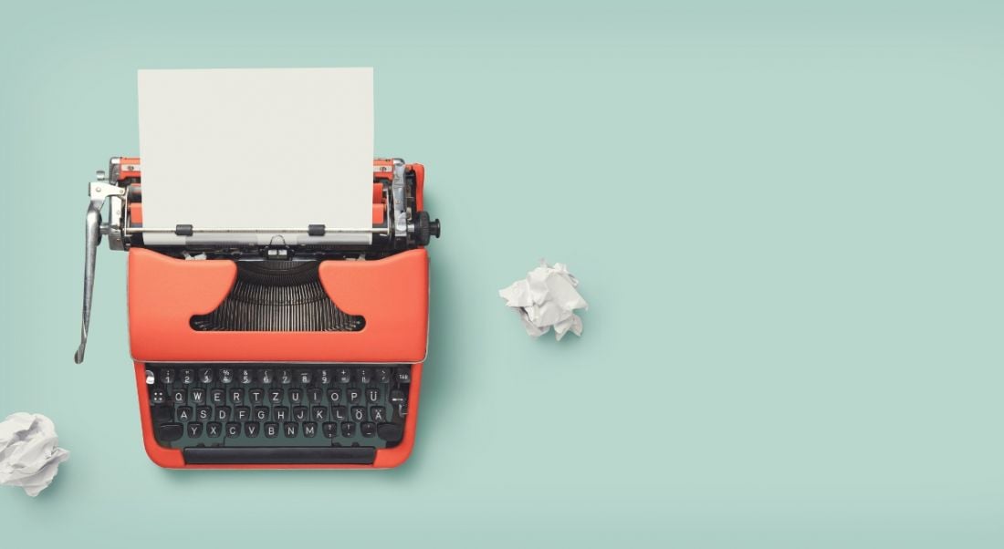 A red vintage typewriter with scrunched up balls of paper against a light blue background.