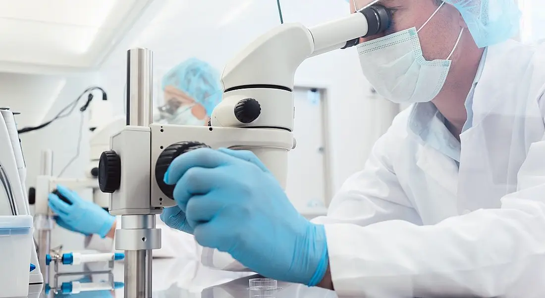 Lab technicians in full PPE working on microscopes.