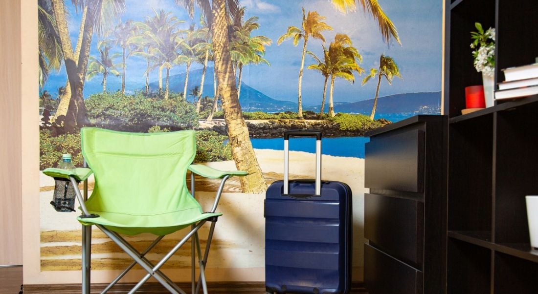 A green chair in an office is in front of a poster of a beach, symbolising a fake Zoom background.