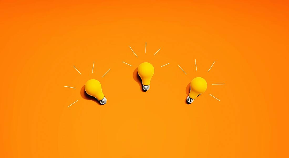 Three yellow lightbulbs are laying against a bright orange background.