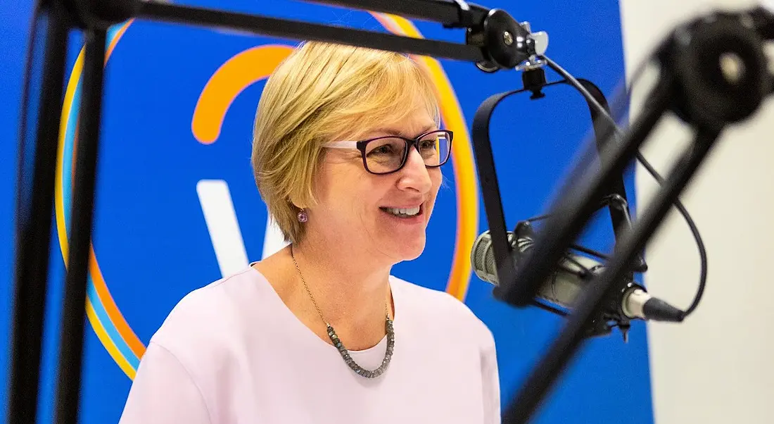 Workday’s Chris Byrne sits at a microphone recording a podcast. The Workday logo is on a screen behind her.