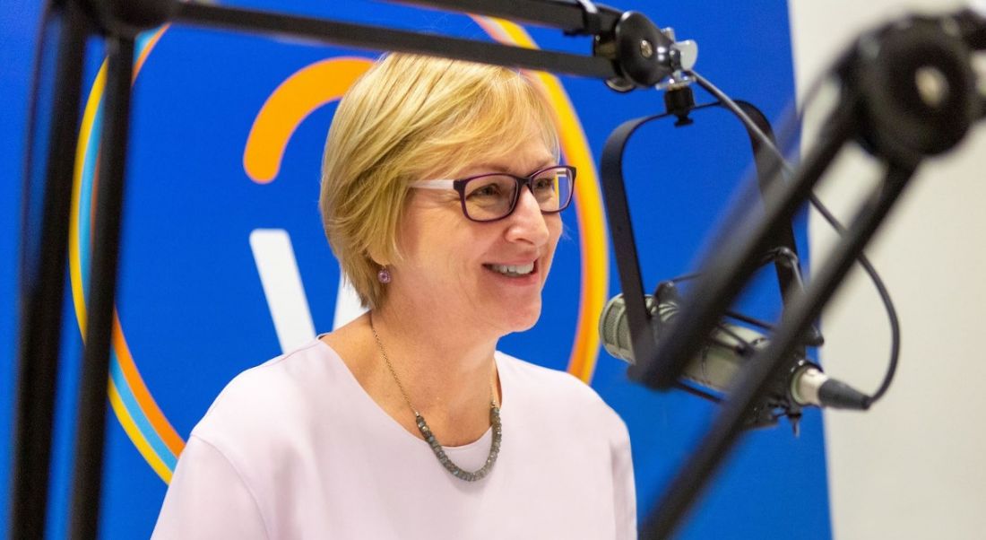 Workday’s Chris Byrne sits at a microphone recording a podcast. The Workday logo is on a screen behind her.