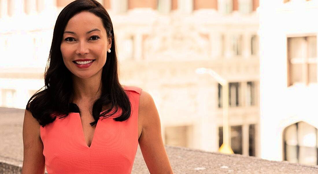 Girls in Tech CEO Adriana Gascoigne is standing outside on a balcony in a bright pink dress, smiling into the camera.