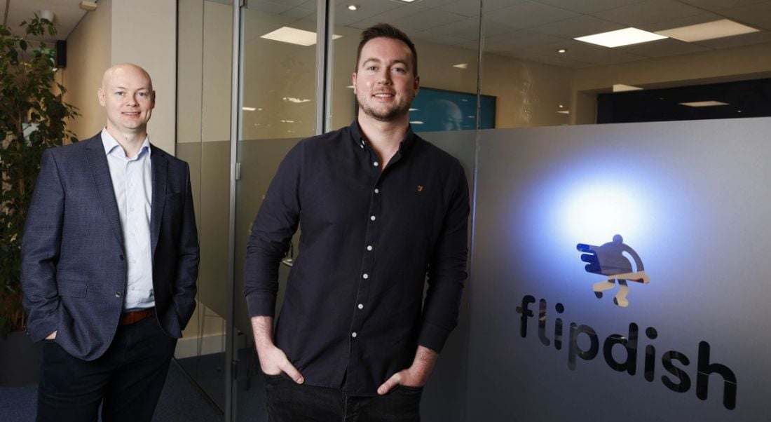 Conor and James McCarthy of Flipdish are standing in an office that has the Flipdish logo on a glass wall beside them. They are smiling into the camera.