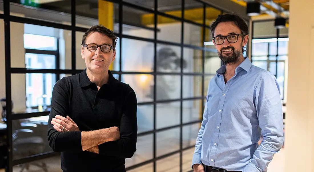 Mammoth co-founders Paul Martin and Jeremy Poots, wearing business-casual attire, stand in a brightly lit office space.