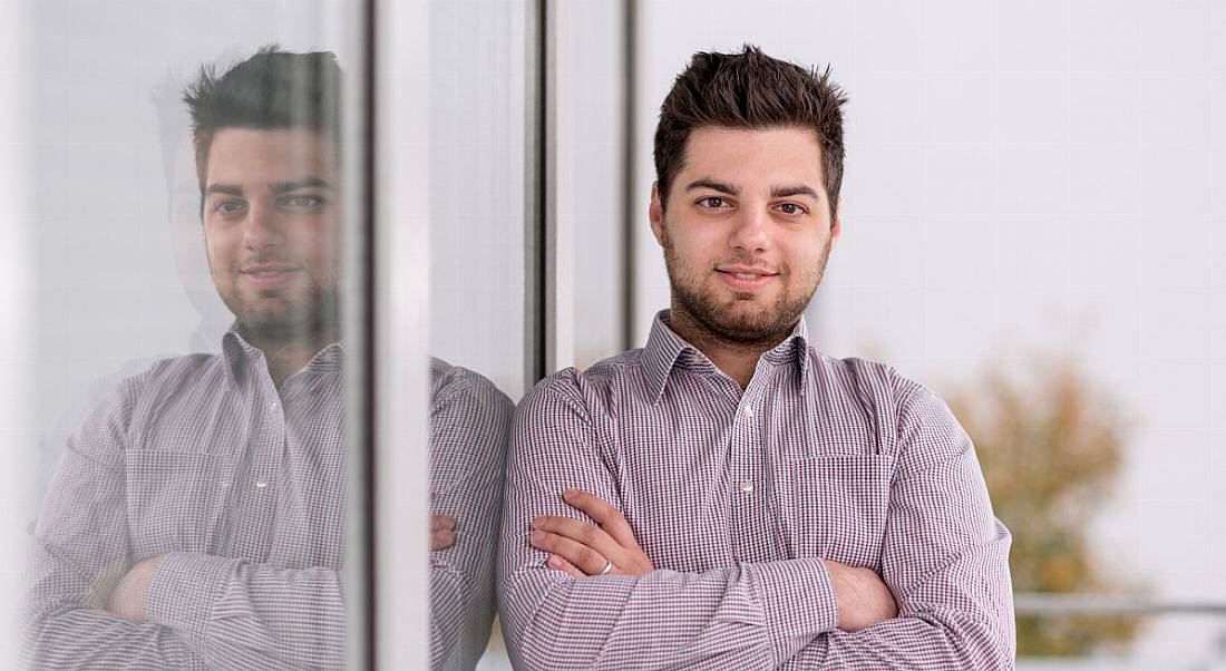 Artur Kane, head of product marketing at Flowmon Networks and NetSecOps expert, is standing against a window showing his reflection with his arms crossed while smiling into the camera.