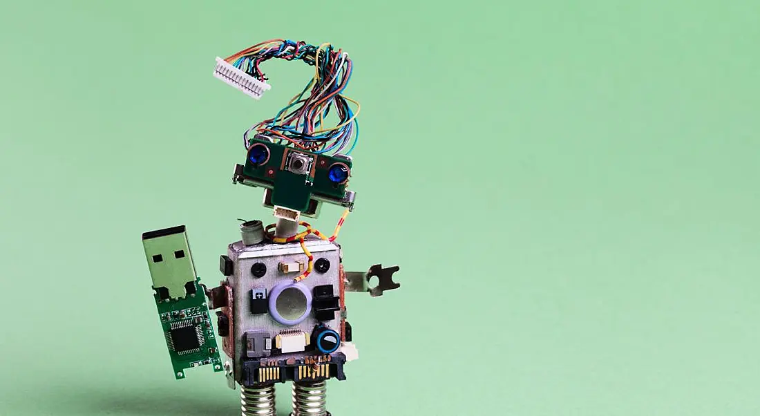 A robot made from electronic components is standing against a light green background.