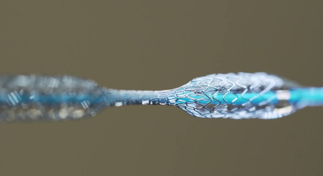 The wire mesh of a stent expanding in parts along a thin blue wire.