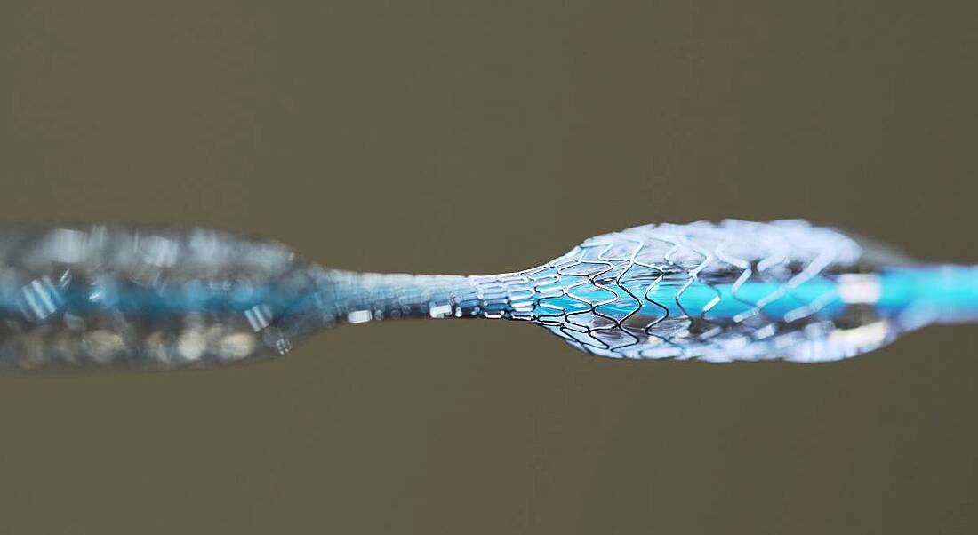 The wire mesh of a stent expanding in parts along a thin blue wire.