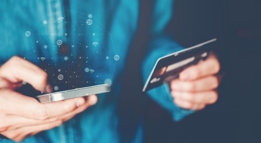 Close-up of a person using a debit card to pay for something on their smartphone.