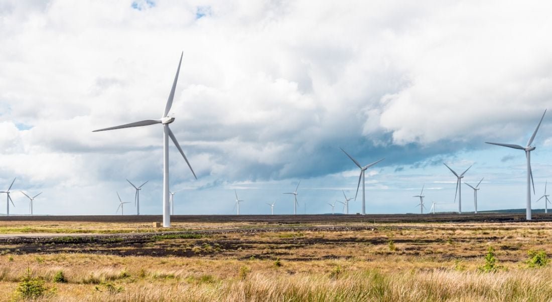 A number of wind turbines dotted across an empty landscape under a cloudy sky.