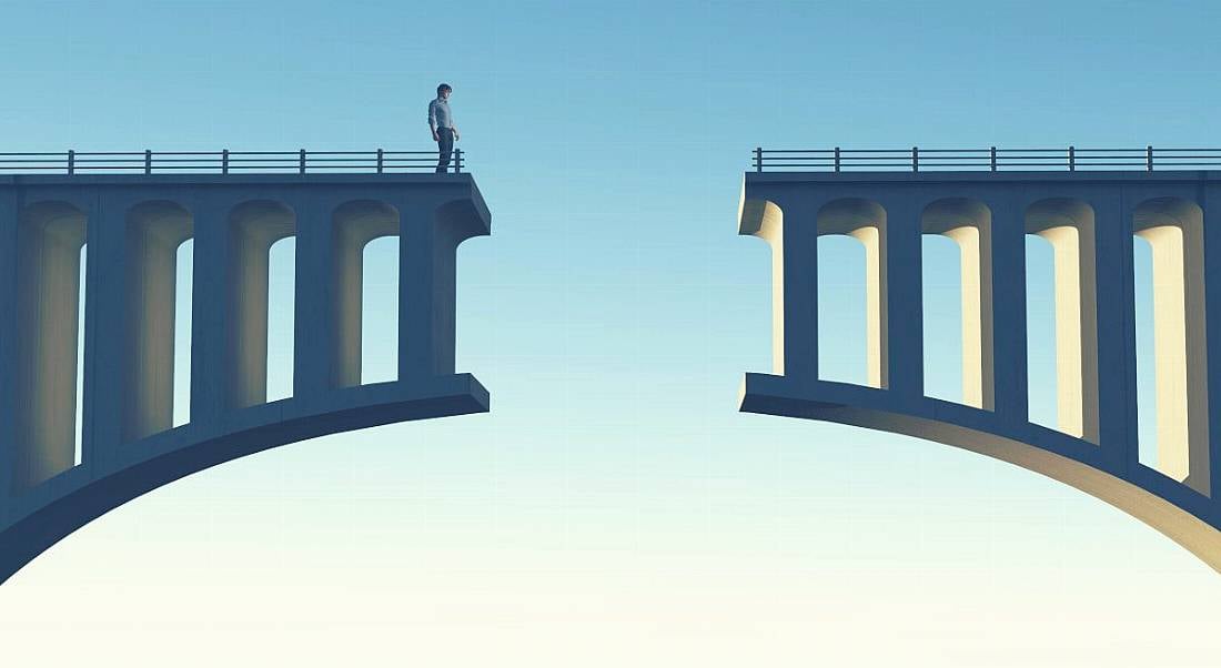 A figure of a person is standing and looking down at a gap in a broken bridge against a blue sky, symbolising a skills gap.