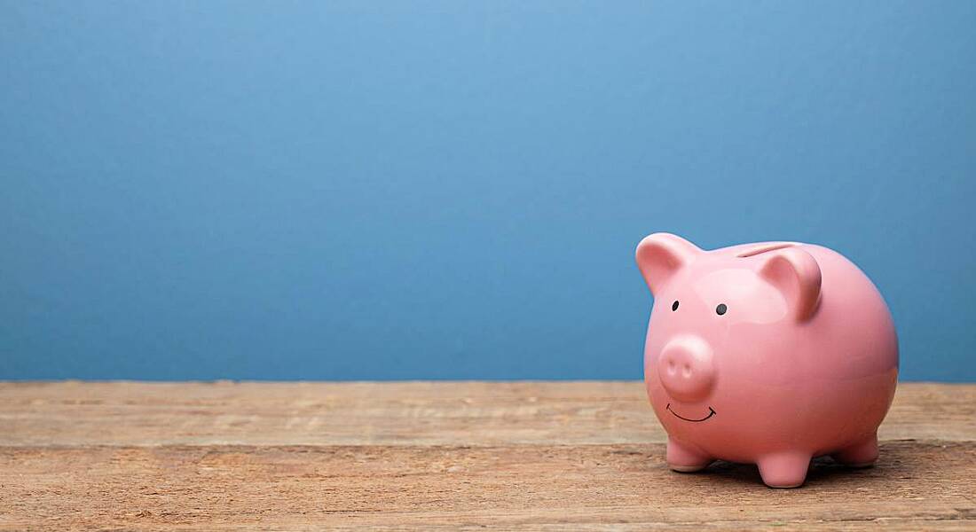 Pink piggy bank on a wooden surface against a blue background.