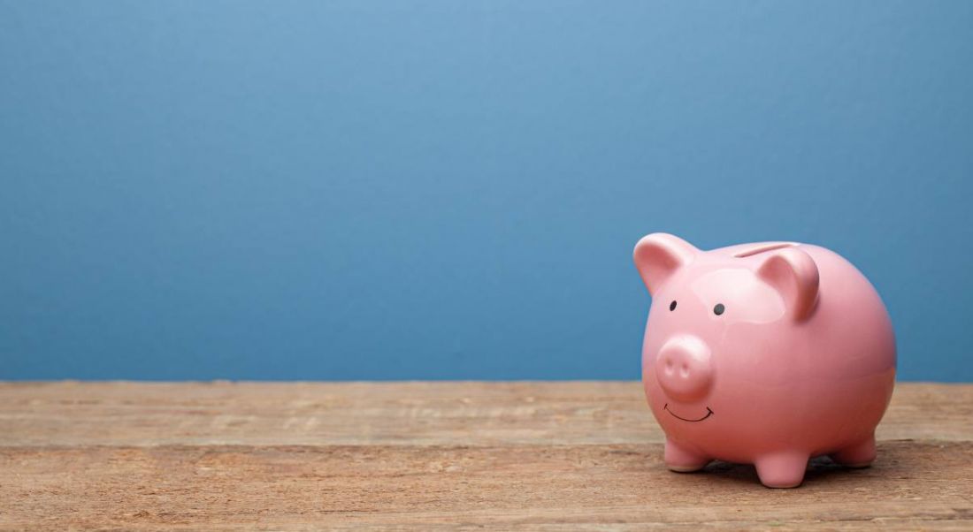 Pink piggy bank on a wooden surface against a blue background.