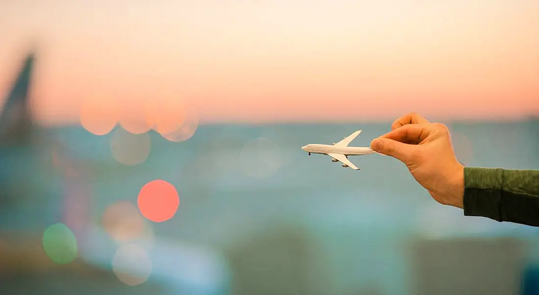 Hands are holding a miniature airplane model up against a blurred background with a sunset.