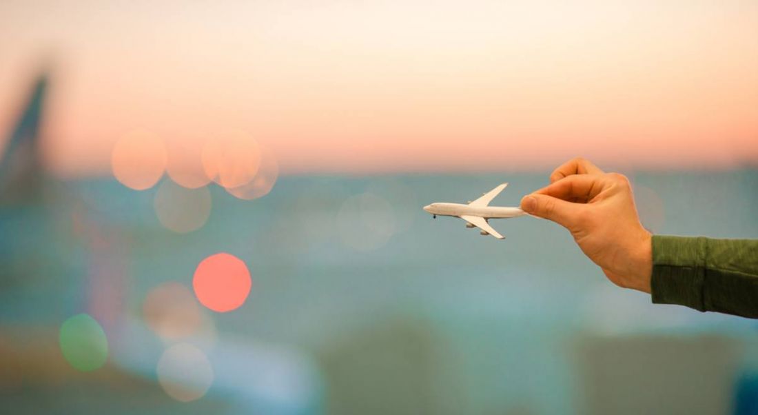 Hands are holding a miniature airplane model up against a blurred background with a sunset.