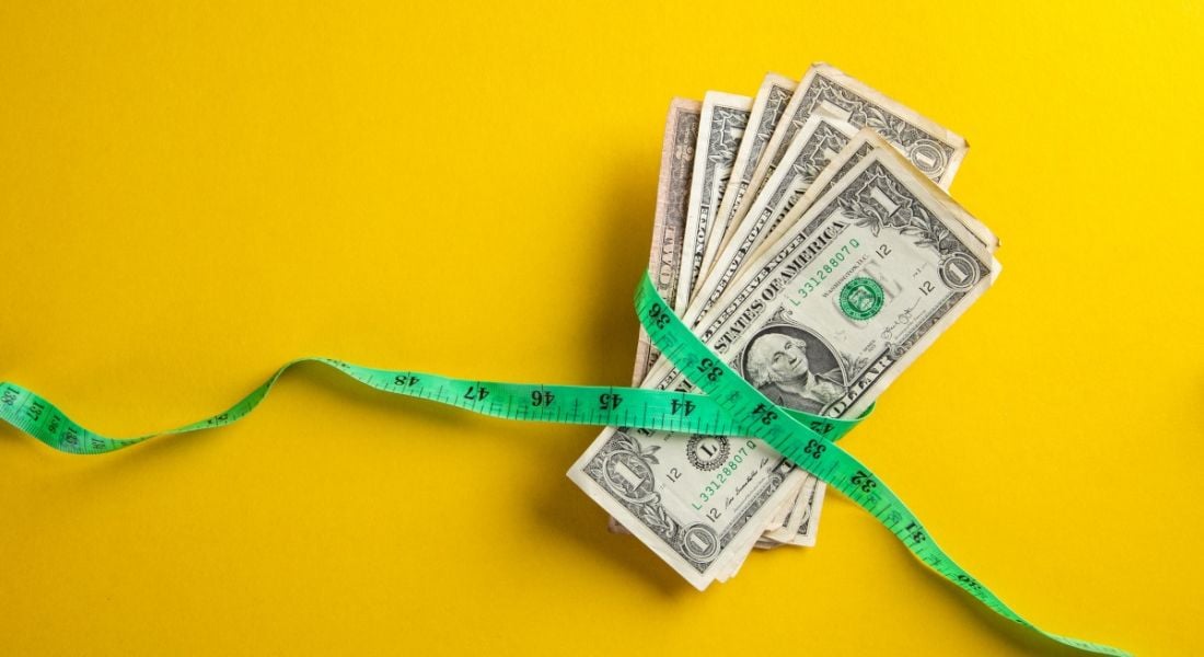 A pile of dollars has a green measuring tape around it on a yellow background.