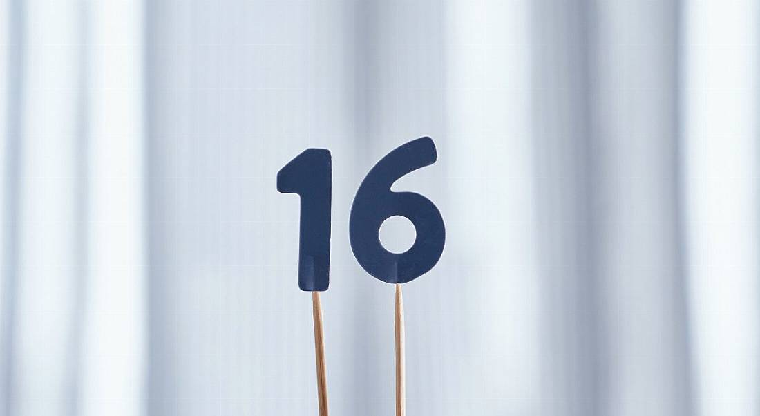 Wooden sticks are holding up the number 16 cut out of blue paper.