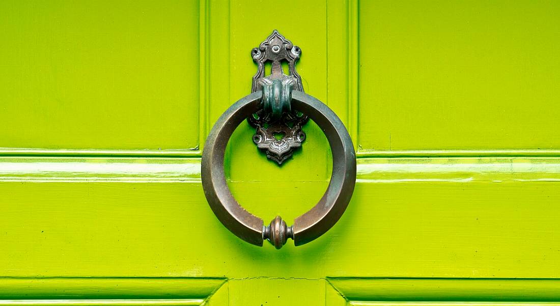 An antique knocker on a lime green wooden door.