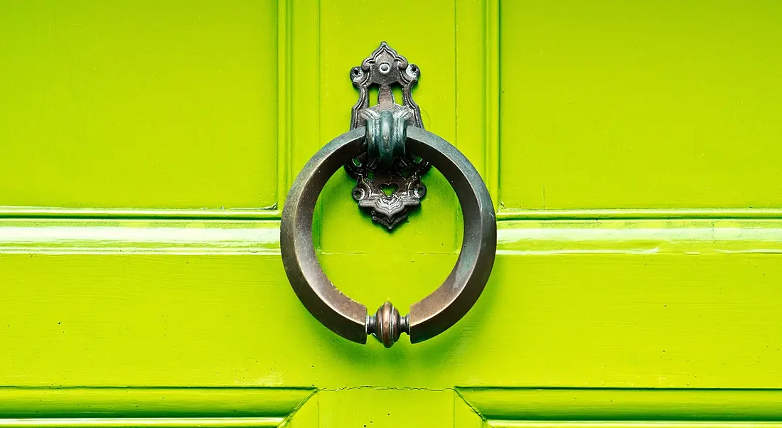 An antique knocker on a lime green wooden door.