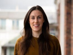 Aoife Dillon of MSD is standing in front of a window and smiling into the camera.