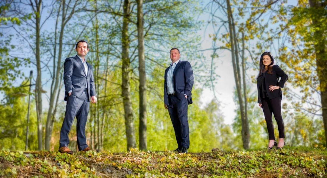 Three people in suits are standing in a wooded area on a bright day for the announcement that Hikari has acquired ProcessUs.