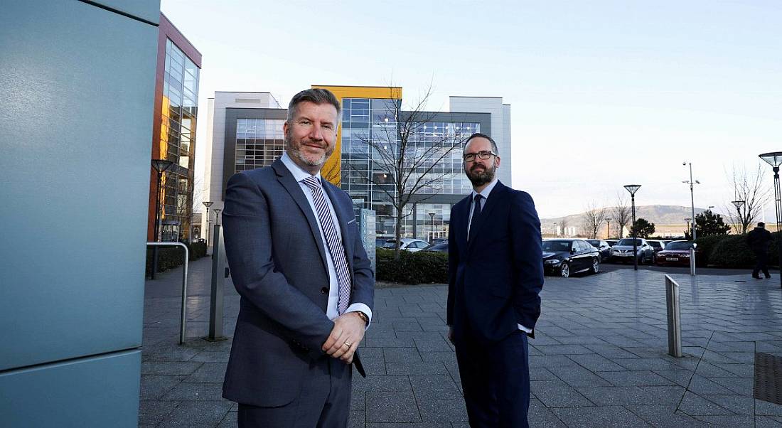 Two men in business suits stand outside the Expleo Northern Ireland headquarters in the Titanic Quarter in Belfast.