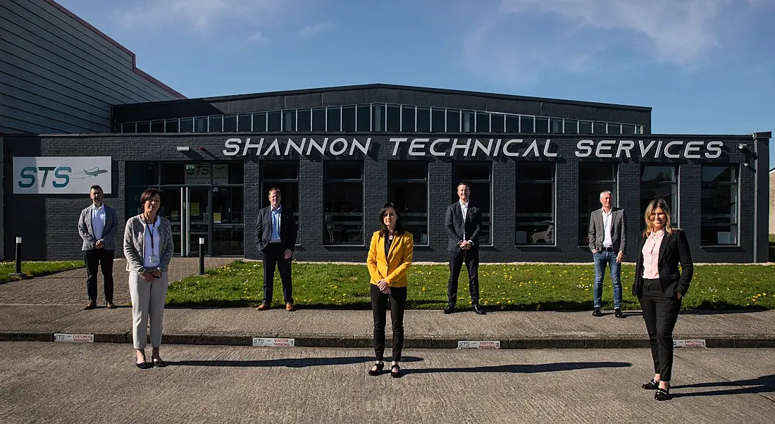 Seven men and women stand a few metres apart outside the Shannon Technical Services building on a sunny day.