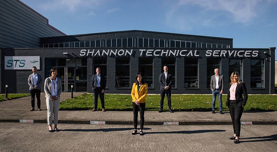 Seven men and women stand a few metres apart outside the Shannon Technical Services building on a sunny day.