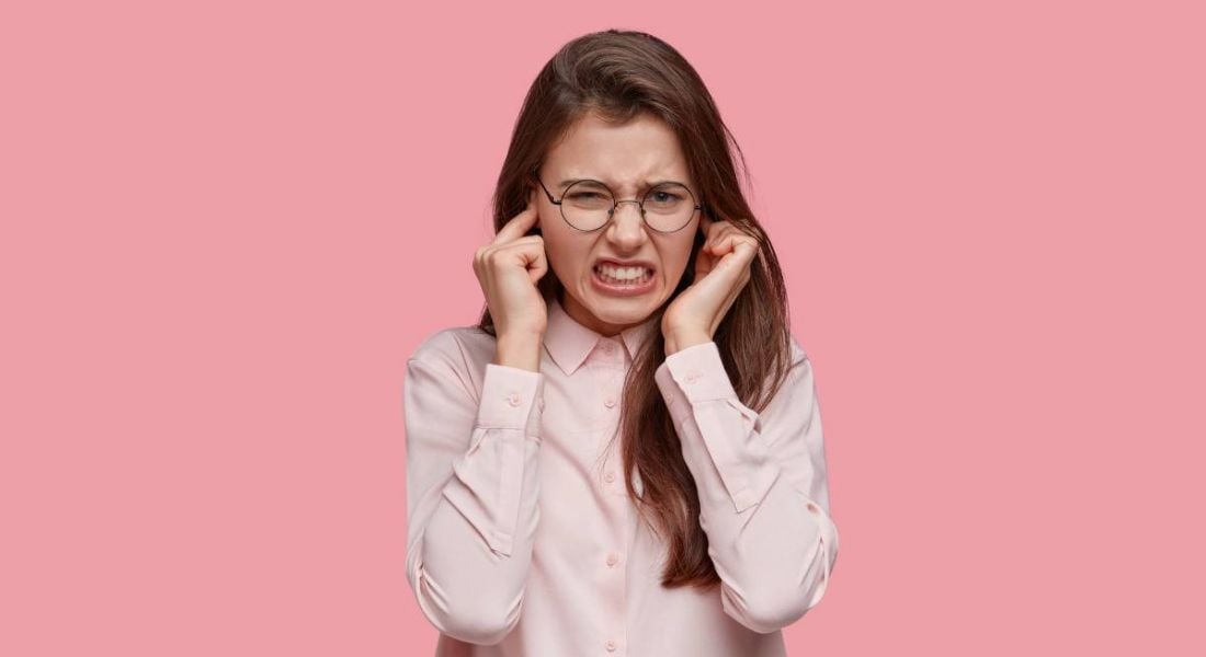 A young woman is blocking her ears so that she cannot hear the most-hated office buzzwords.