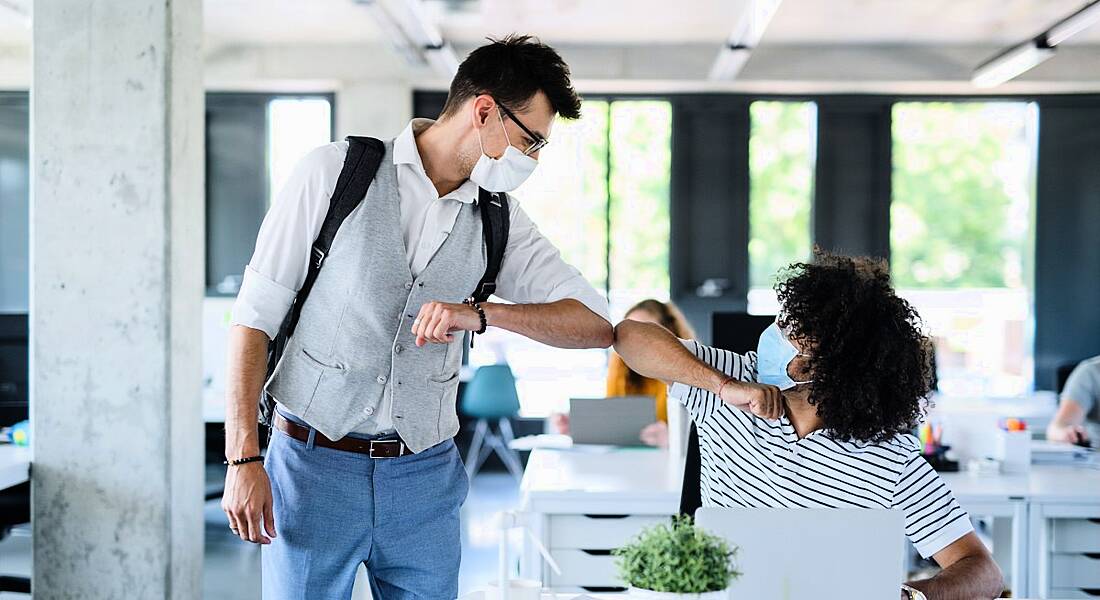Employees in a bright, modern workplace are bumping elbows while wearing masks as they return to work in line with Government safety measures.