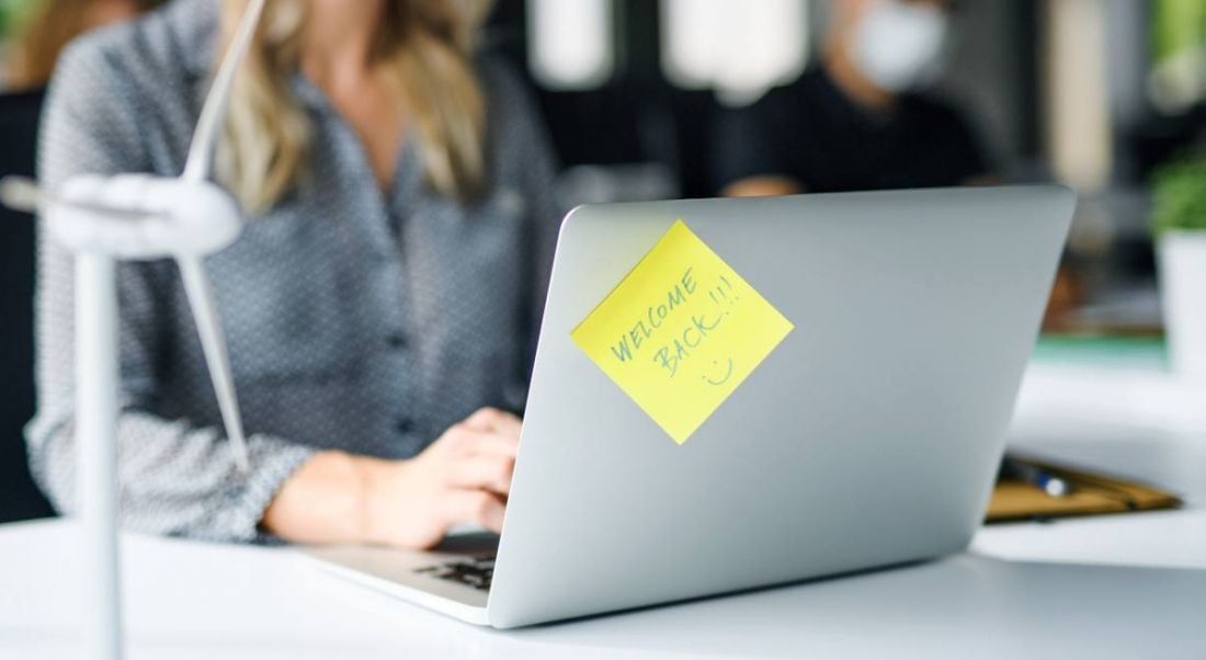 Close-up of a post-it note on a laptop that says 'welcome back' on it.