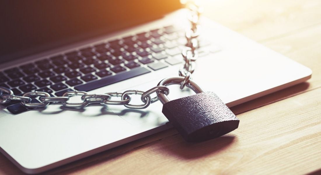 A grey padlock and chain lie across a laptop keyboard, representing cybersecurity.