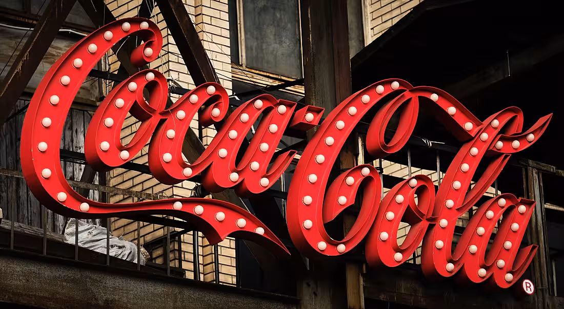 Large 3D sign of the Coca-Cola logo on the side of building.