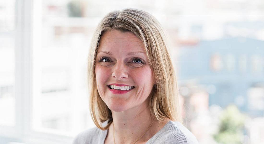 Zoë Harte of Upwork is smiling into the camera in front of a window in a brightly lit room.