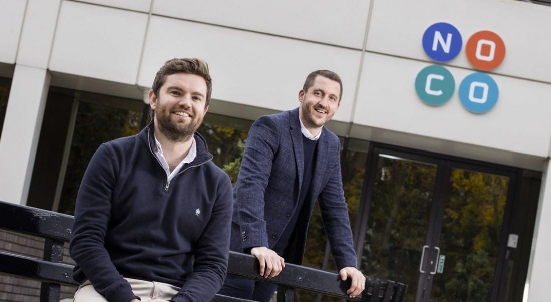 Two men stand outside an office that says 'NoCo' on the side.