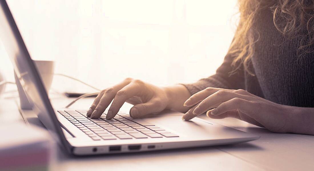 A close-up of a person’s hands working on a laptop in a brightly lit room.